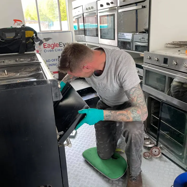 A trainee kneeling to remove an oven door in the training workshop