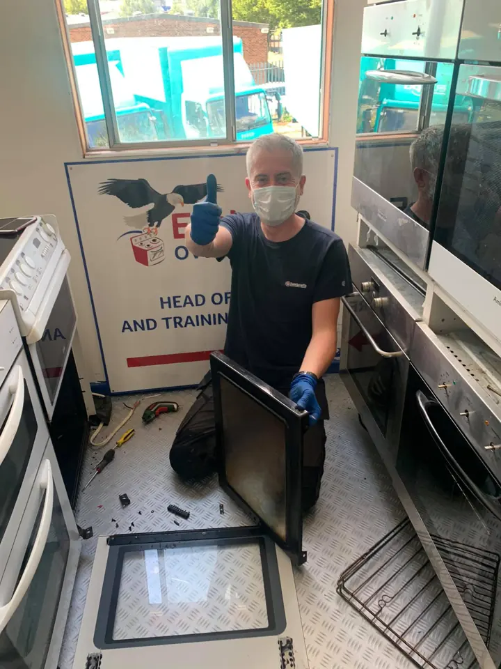 A trainee in the workshop van giving a thumbs up next to an oven door